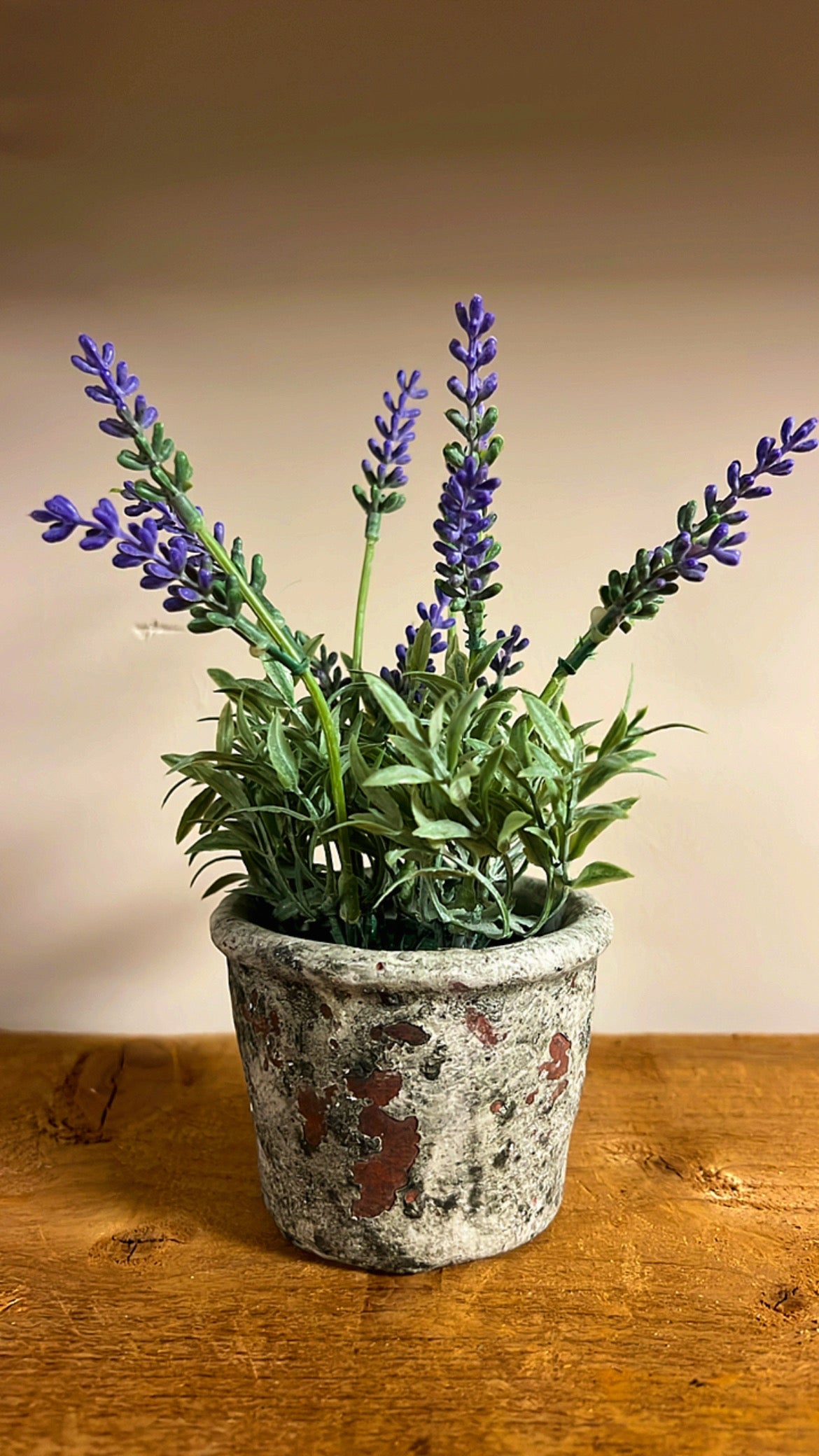 Kunst lavendelplant met paarse bloemen, geplaatst in een rustieke vintage pot, op een houten tafel.