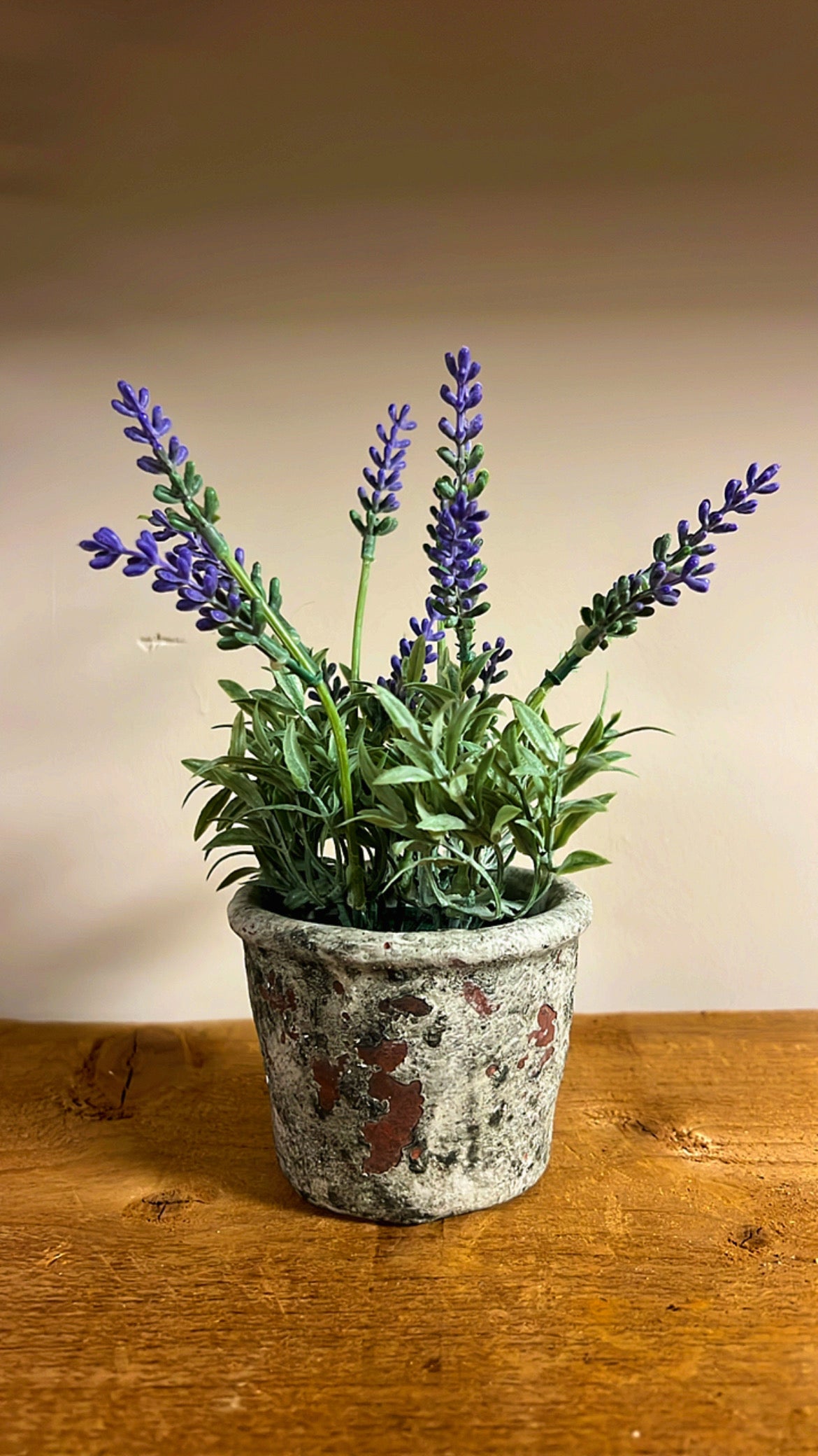 Kunst lavendelplant met paarse bloemen, geplaatst in een rustieke vintage pot, op een houten tafel.