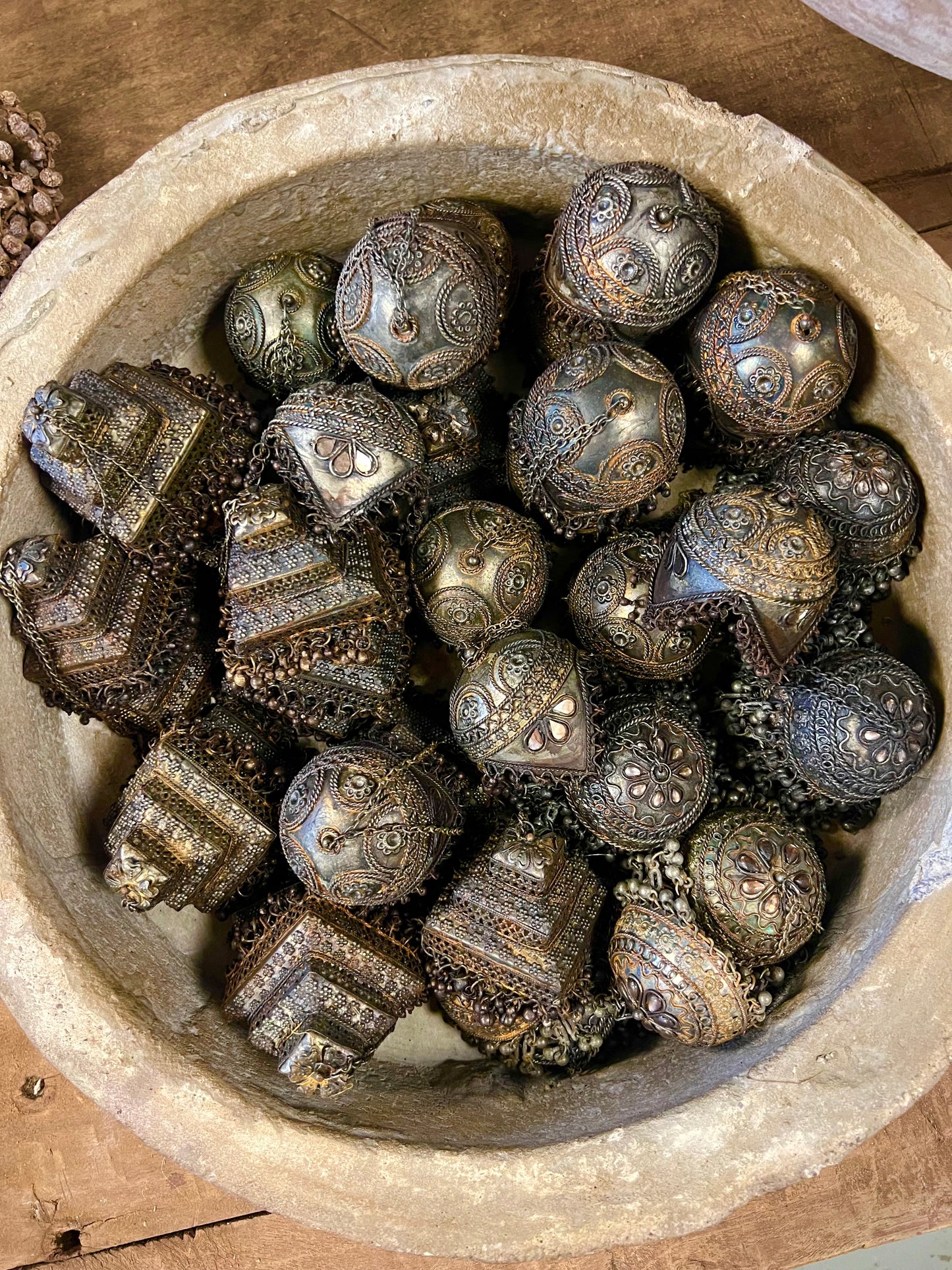 Drie decoratieve metalen ornamenten in de vorm van belletjes, versierd met details, in een rustieke betonnen schaal.