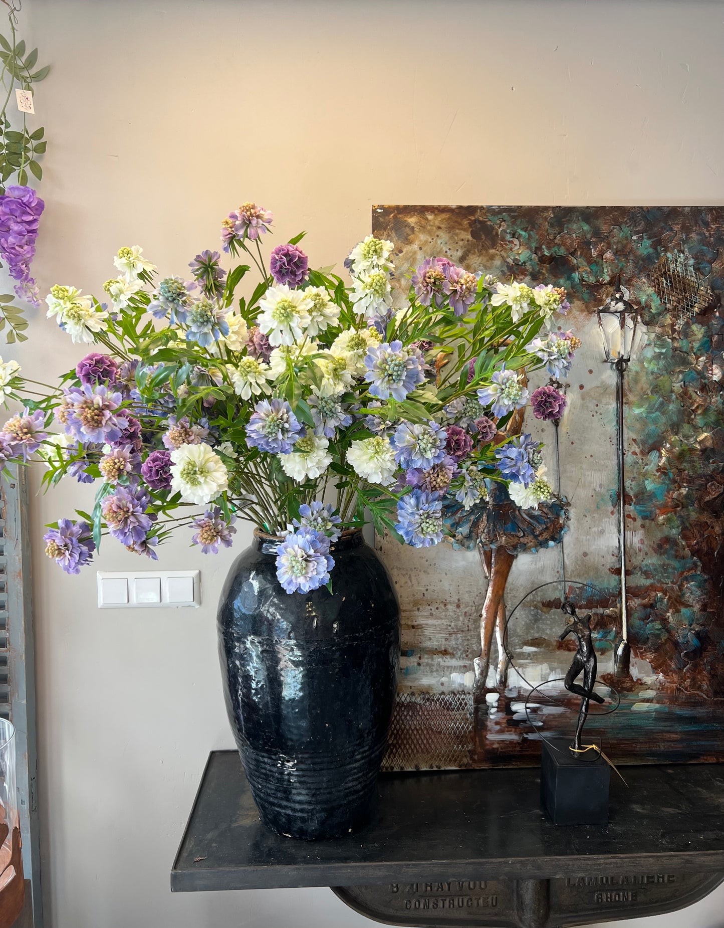 Zijden boeket met lila, paarse en witte bloemen in een zwarte vaas, geplaatst op een tafel.
