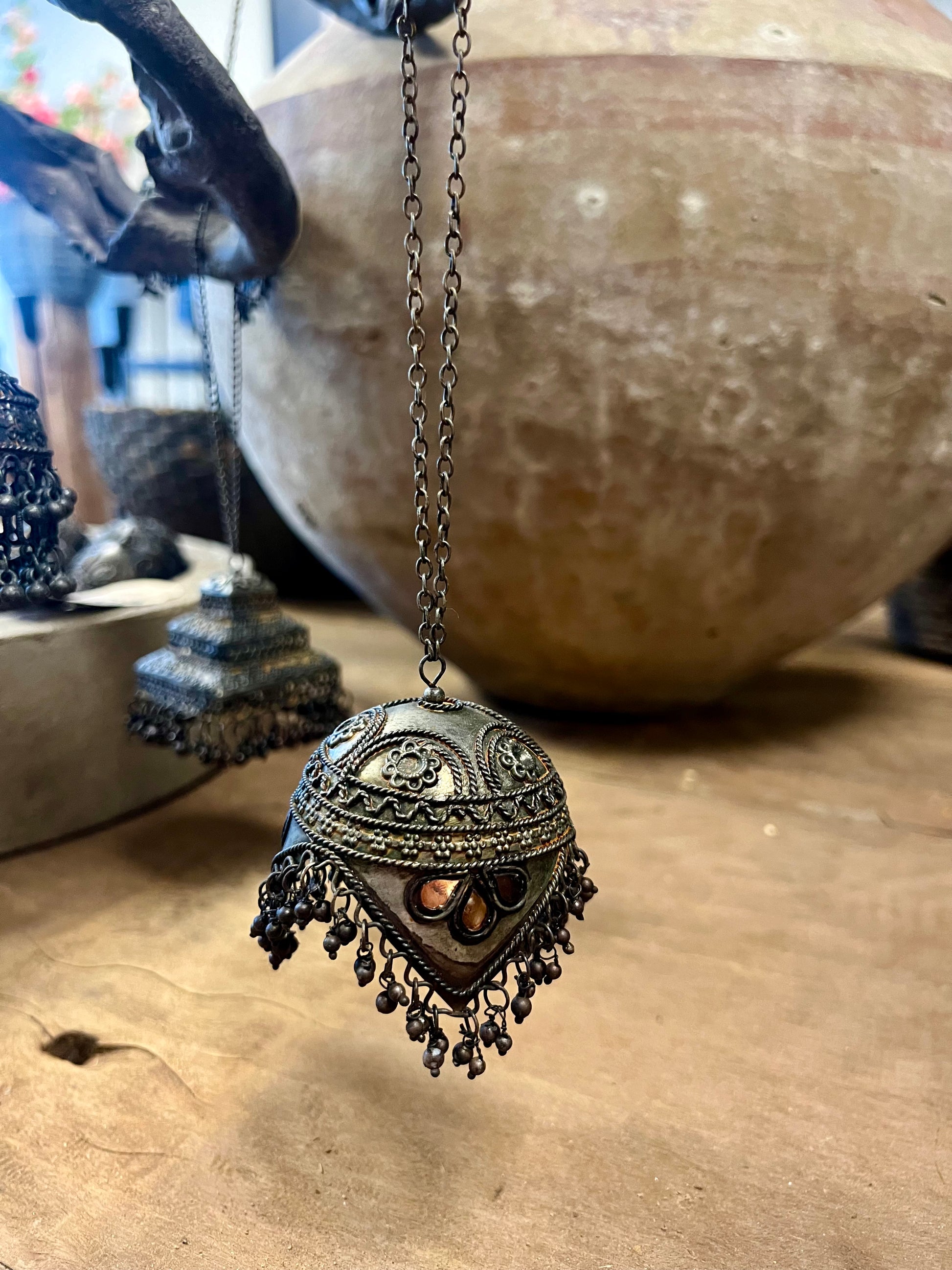 Drie decoratieve metalen ornamenten in de vorm van belletjes, versierd met details, opgehangen aan een tak in een rustieke omgeving.